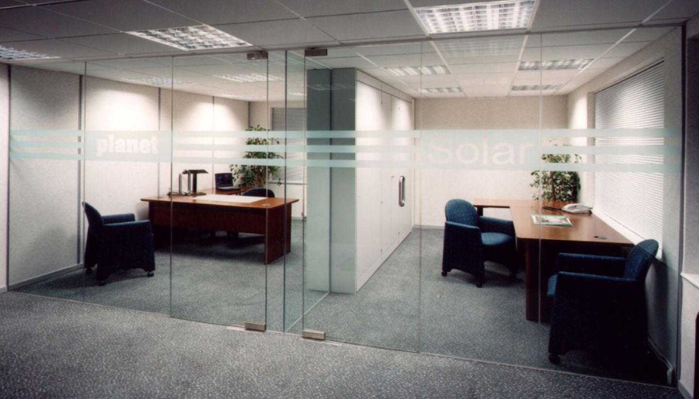 Modern office with glass walls by Factory Direct Glass & Mirror, featuring two desks, chairs, and plants for a clean, professional setting. Experience premium Glass & Mirror Services that elevate your workspace's style and functionality.