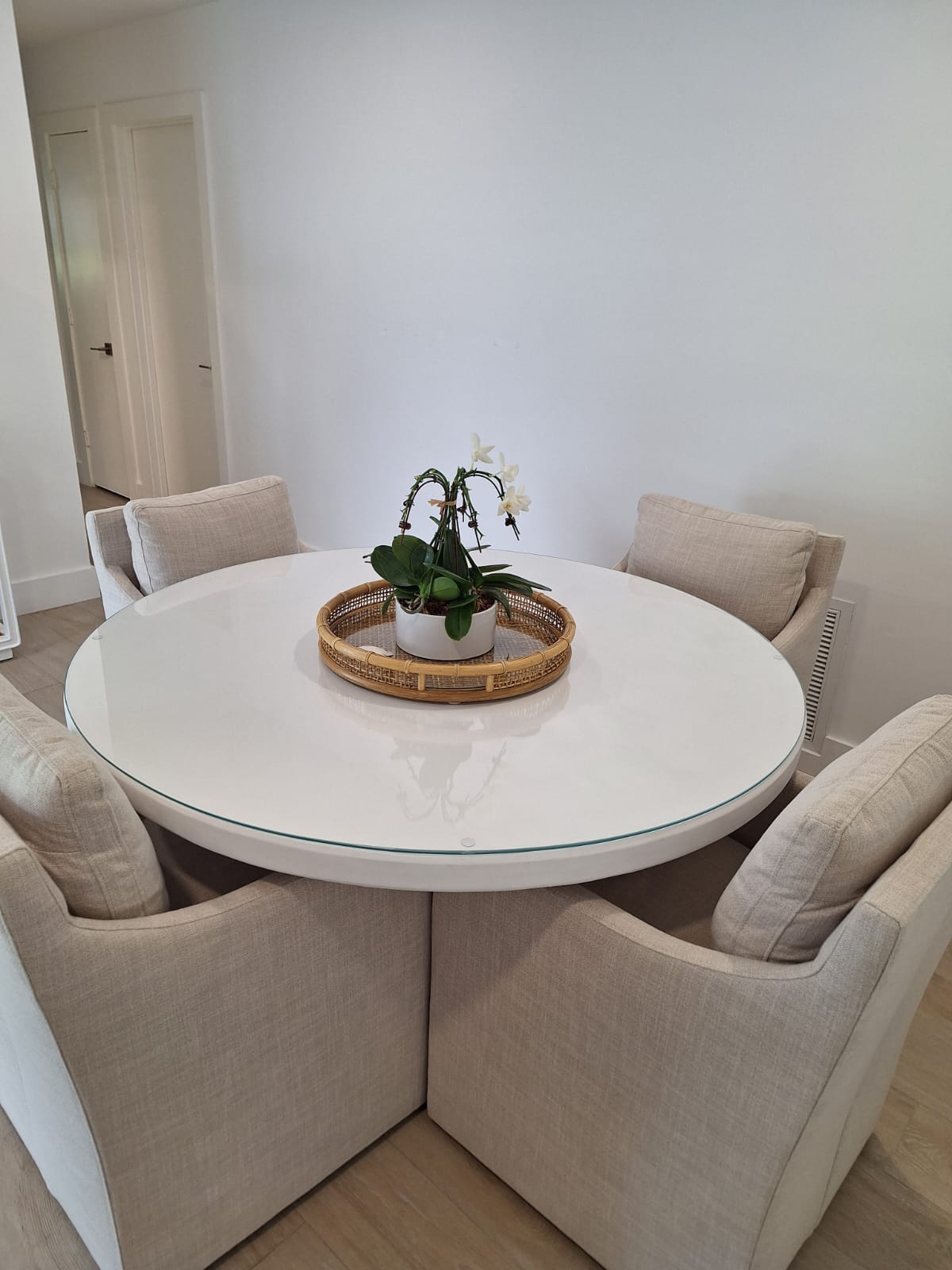 Beige chairs surround a white round table with a potted plant centerpiece in a bright room.