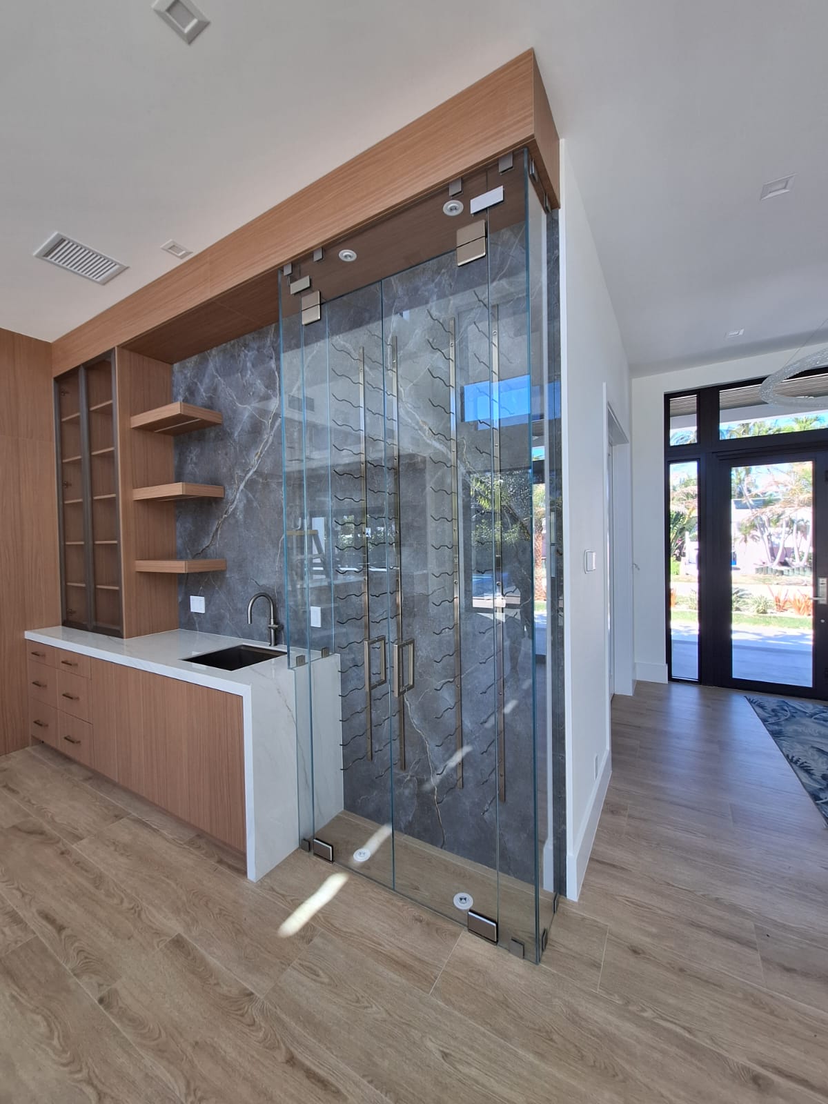 Modern kitchen with wood finishes, a sink, open shelves, and a glass-enclosed wine storage area.