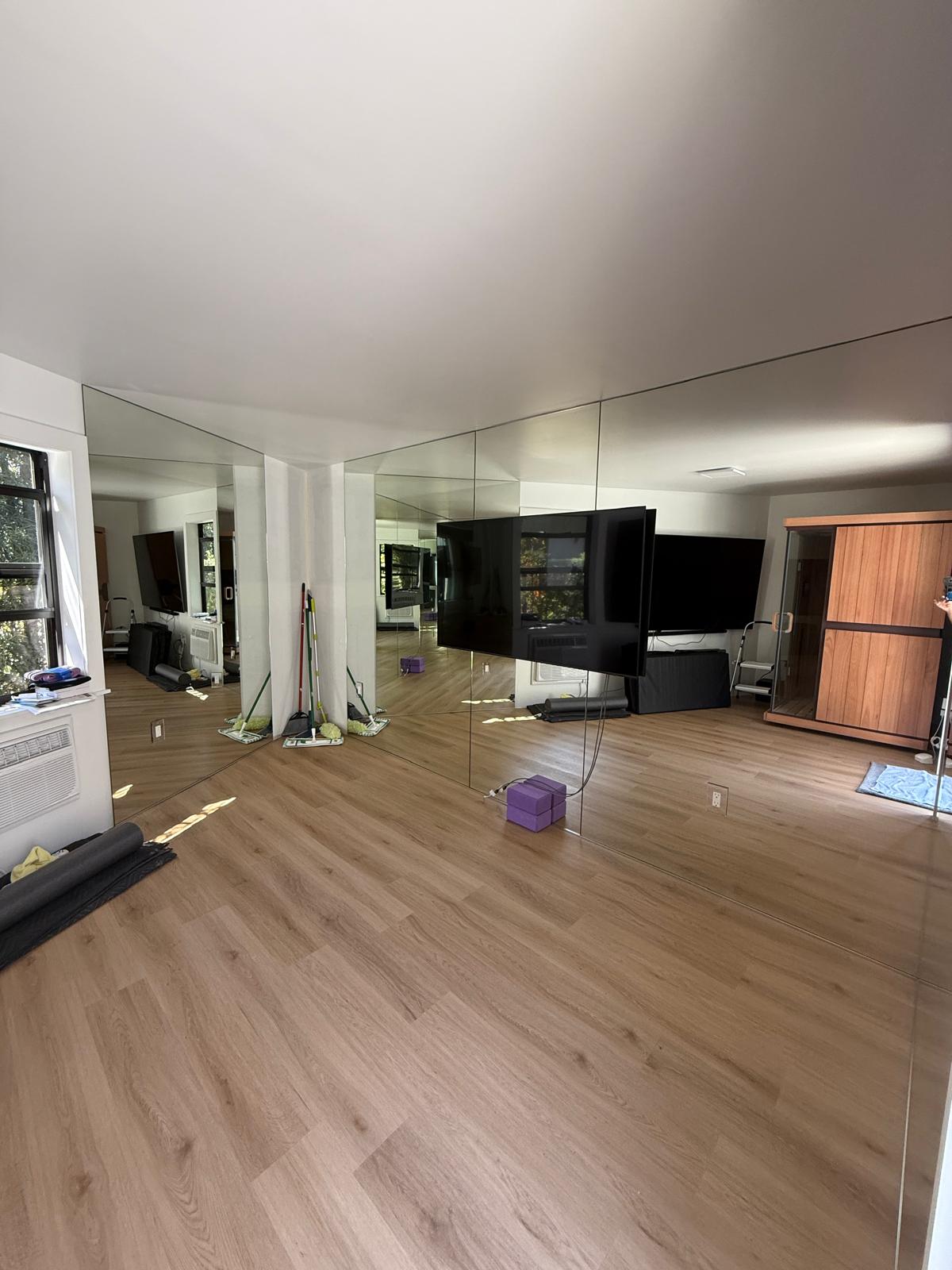 A spacious, empty room with wood floors, mirrored walls, a TV, and cleaning supplies in the corner.