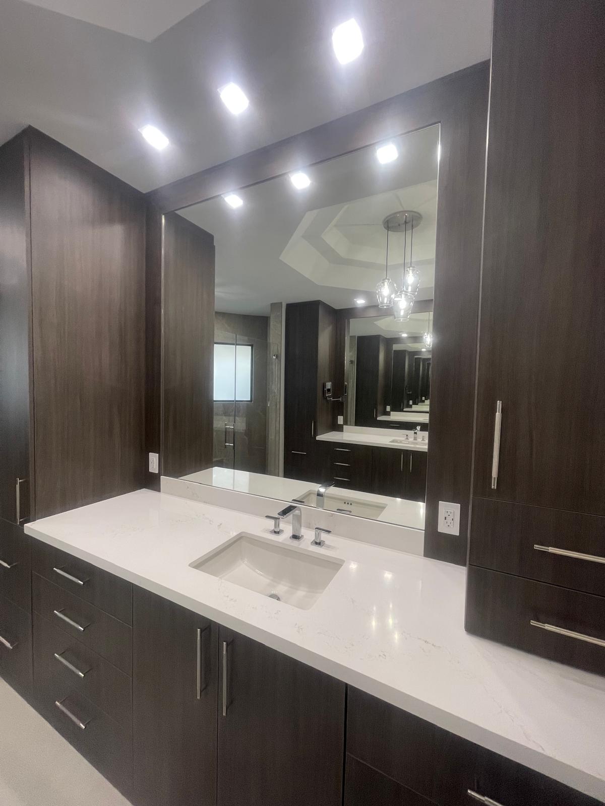 IMG-20250801-WA0004 Modern bathroom with dark wood cabinets, a large mirror, and white countertop with built-in sink.