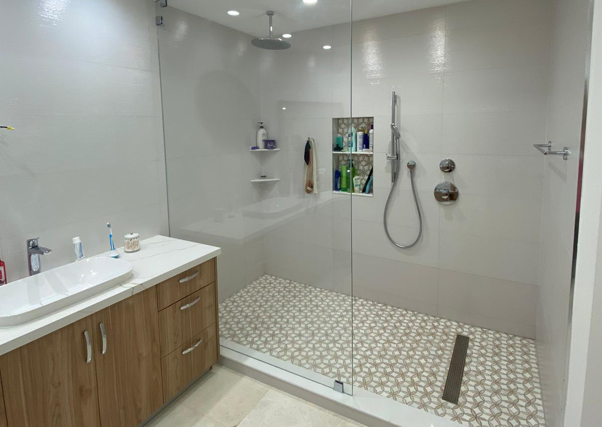 Modern bathroom with a walk-in glass shower, patterned tile floor, and wooden vanity with sink.