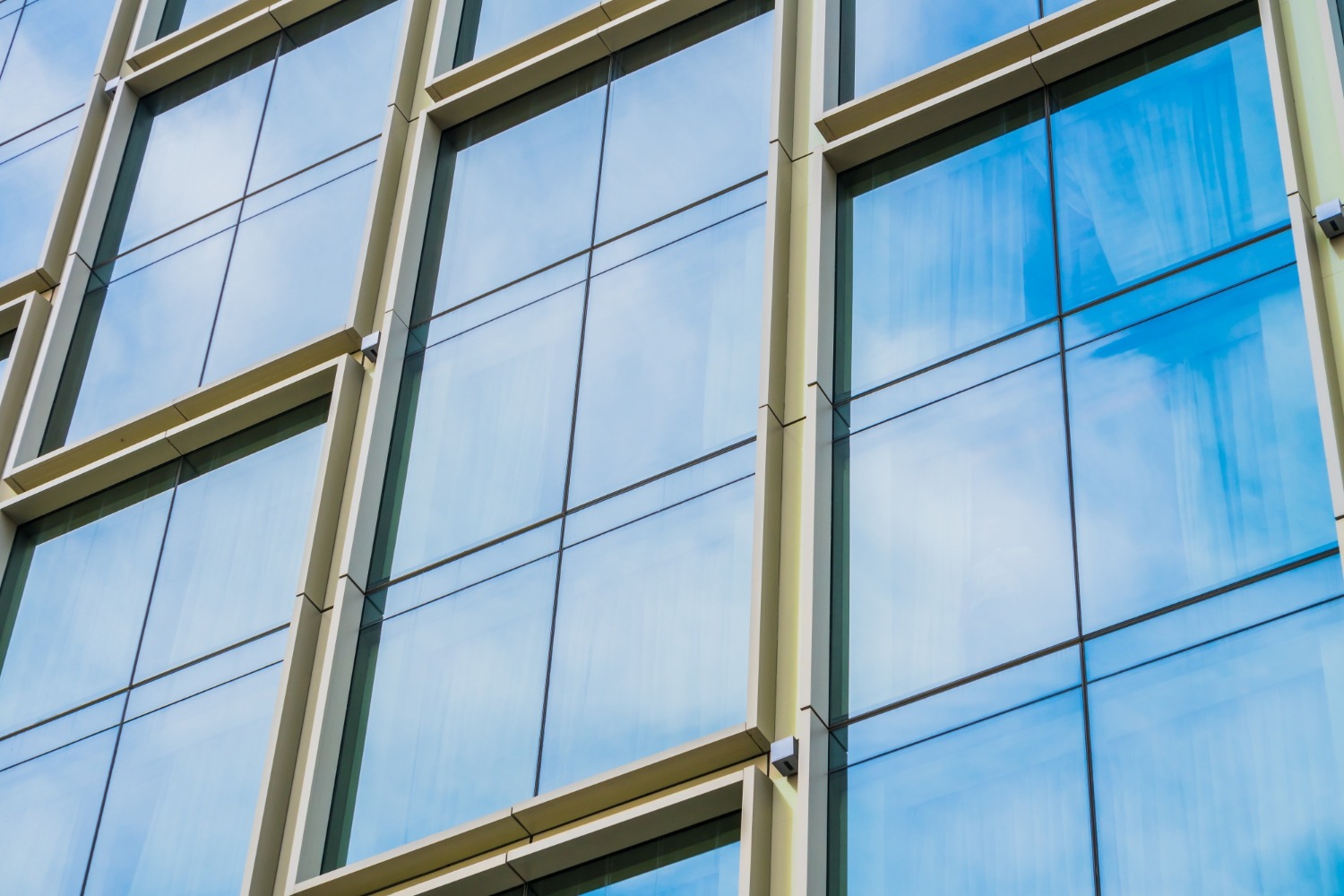 Close-up of modern building facade with expansive window glass reflecting blue sky and clouds.